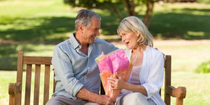 A mature couple sharing flowers on a park bench